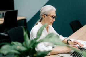 Femme âgée confiante avec des lunettes travaillant sur un ordinateur portable dans un environnement de bureau moderne.