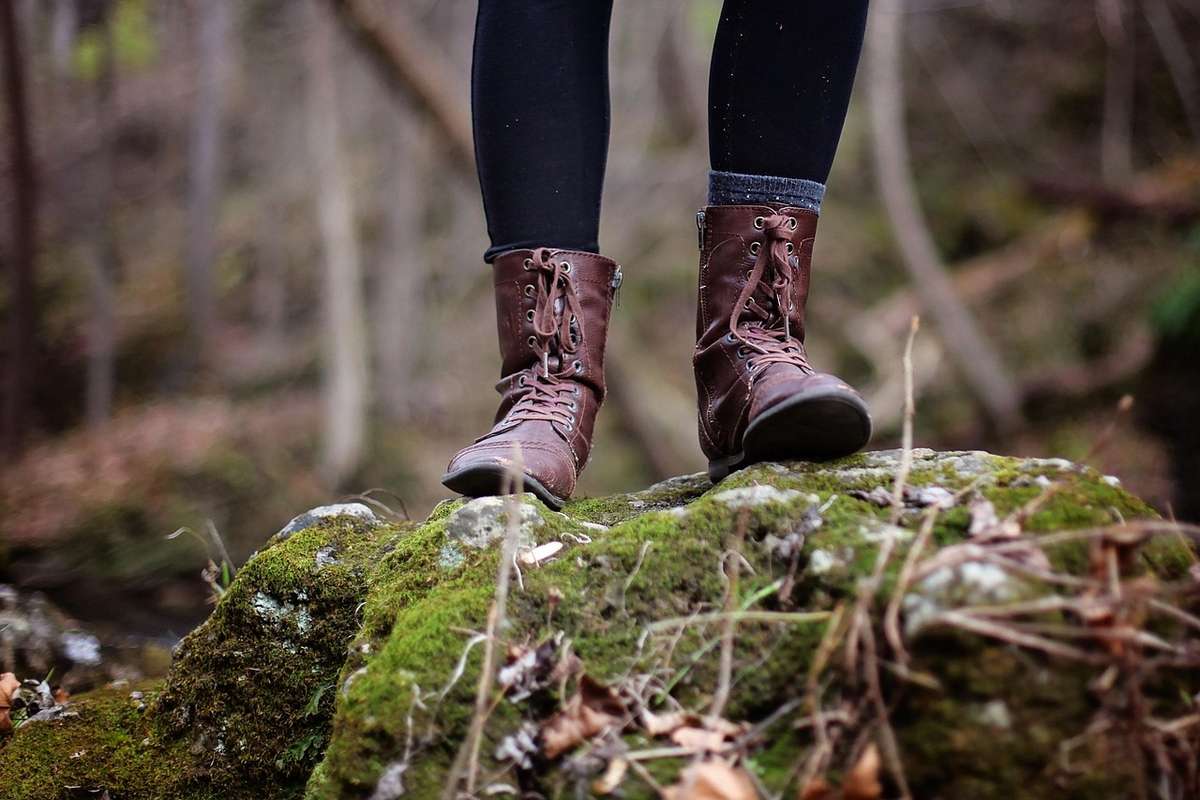 Pieds chaussés de bottes de randonnée sur un tronc recouvert de mousse en forêt Pieds chaussés de bottes de randonnée sur un tronc recouvert de mousse en forêt