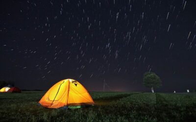 Tente de camping jaune éclairée de l'intérieur sous un ciel nocturne étoilé, en pleine nature