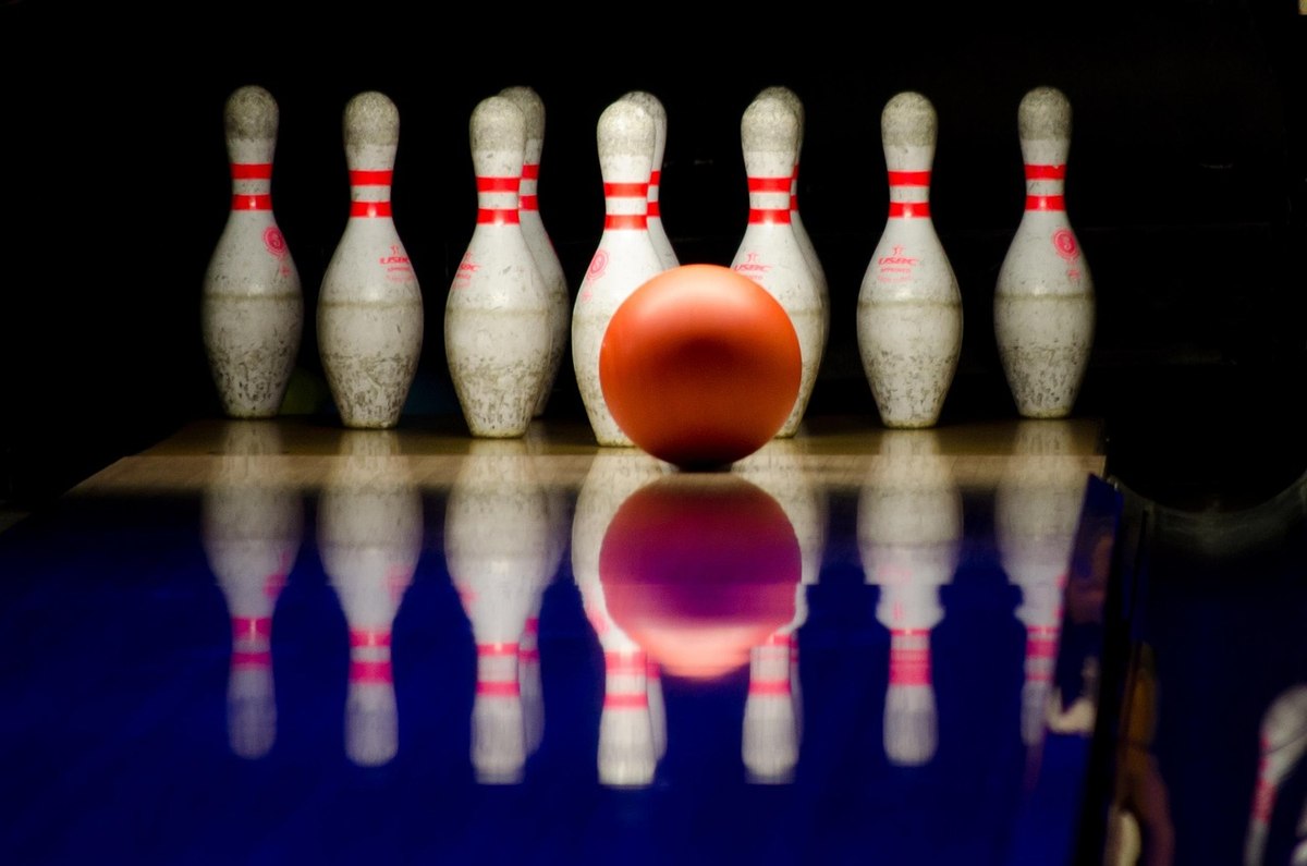 Des quilles blanches et une balle orange sur une piste brillante