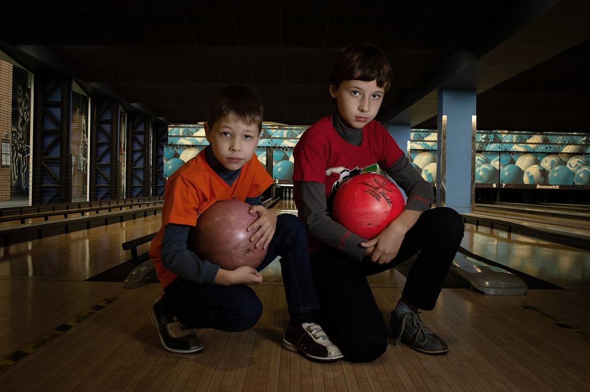 Deux garçons accroupis dans une salle de bowling, tenant des boules Deux garçons accroupis dans une salle de bowling, tenant des boules