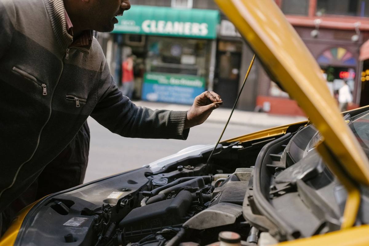Homme vérifie le moteur d'une voiture jaune stationnée près d'un nettoyage Homme vérifie le moteur d'une voiture jaune stationnée près d'un nettoyage