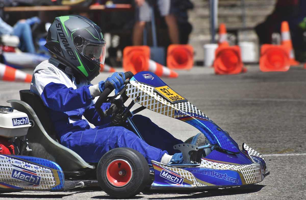 Un conducteur en kart bleu et casque pilote sur circuit avec cônes